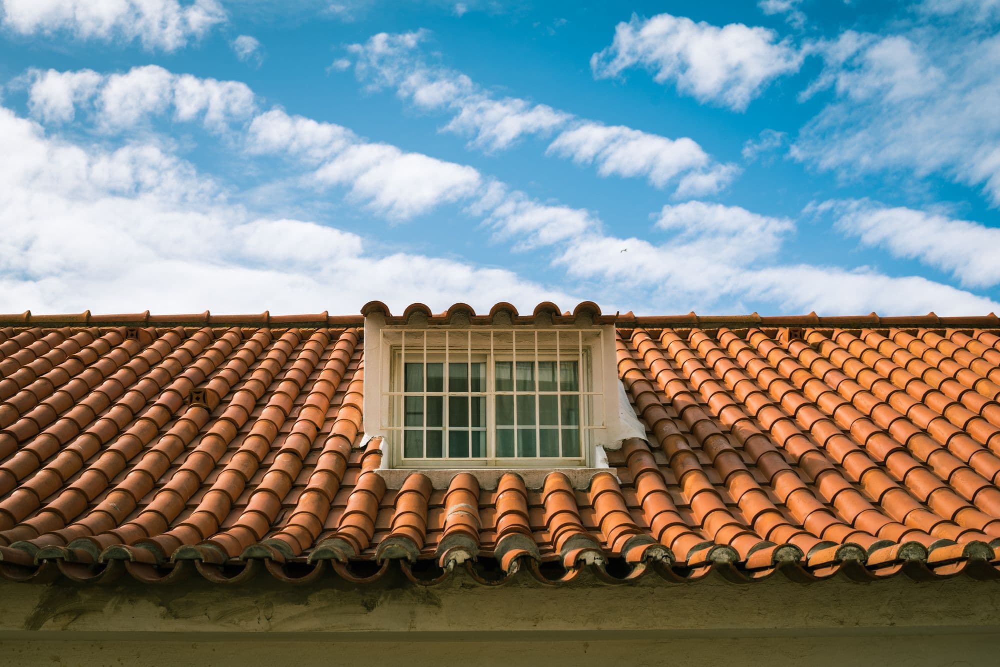 Barrel tile roof and a dormer window against a clear blue sky